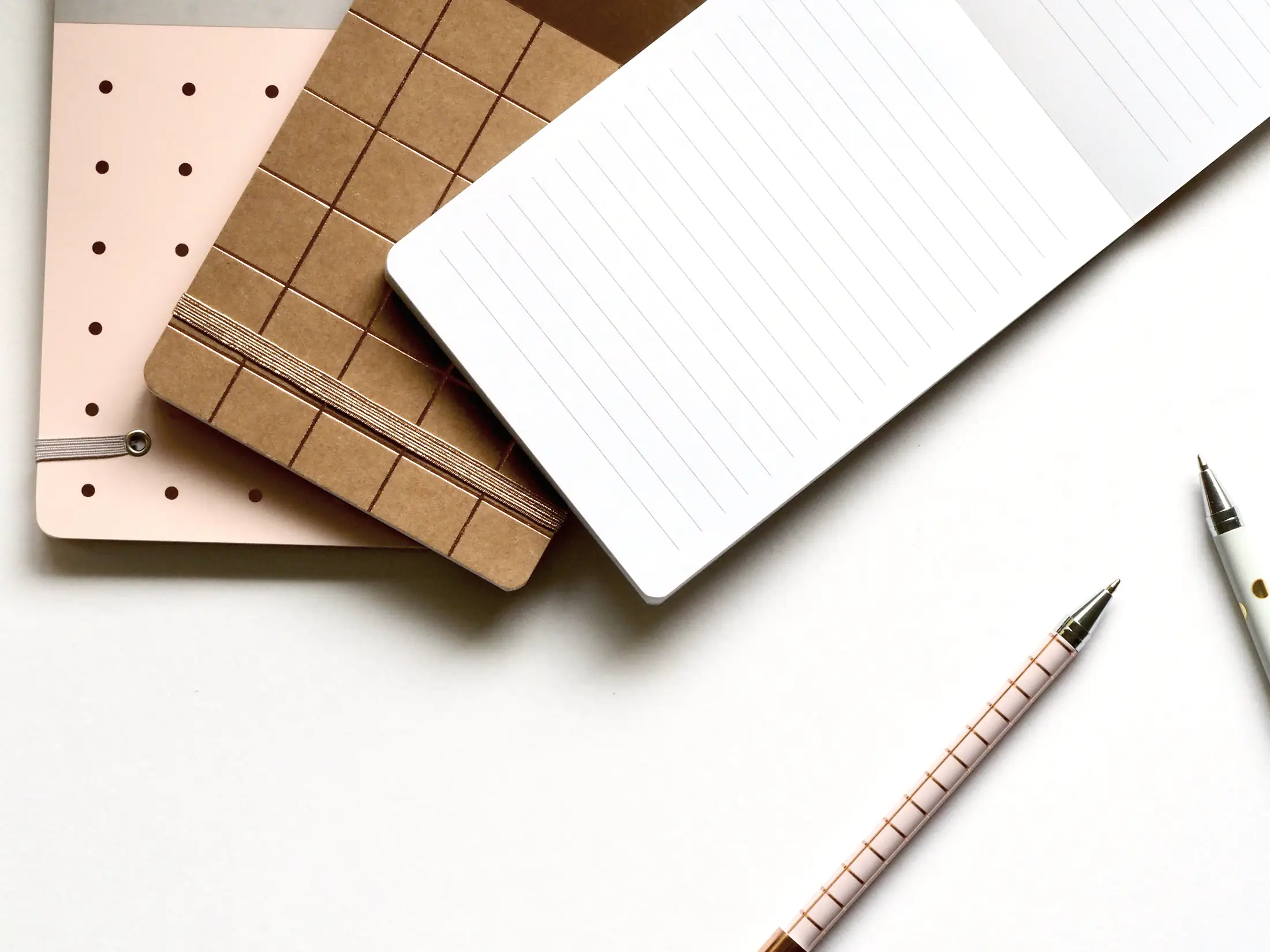 Three different notebooks and a pencil on a white desk